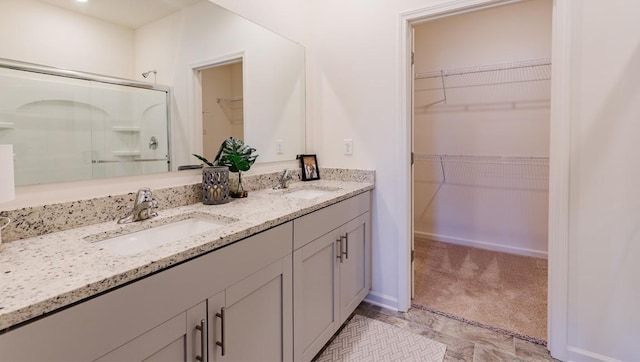 bathroom with double vanity, a shower stall, a spacious closet, and a sink