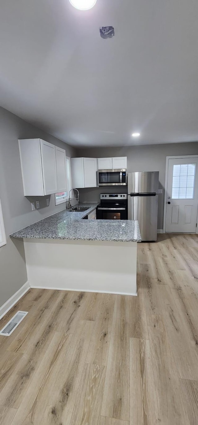 kitchen featuring stainless steel appliances, visible vents, white cabinetry, light wood-type flooring, and light stone countertops