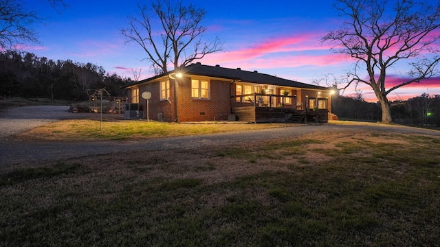 view of side of home with covered porch, brick siding, a yard, driveway, and crawl space