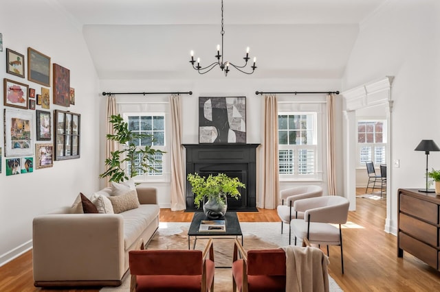 living area featuring an inviting chandelier, a fireplace with flush hearth, vaulted ceiling, and wood finished floors