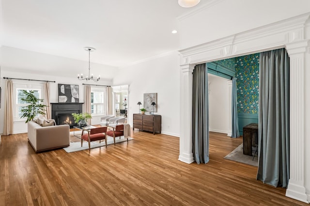 living area featuring a notable chandelier, a lit fireplace, baseboards, and wood finished floors