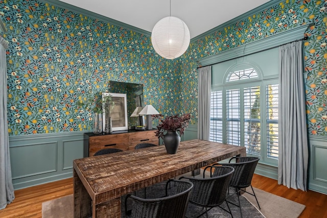 dining room with wallpapered walls, wood finished floors, crown molding, and wainscoting