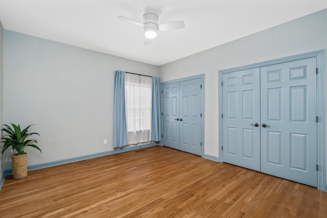 unfurnished bedroom featuring light wood-style flooring, baseboards, ceiling fan, and multiple closets