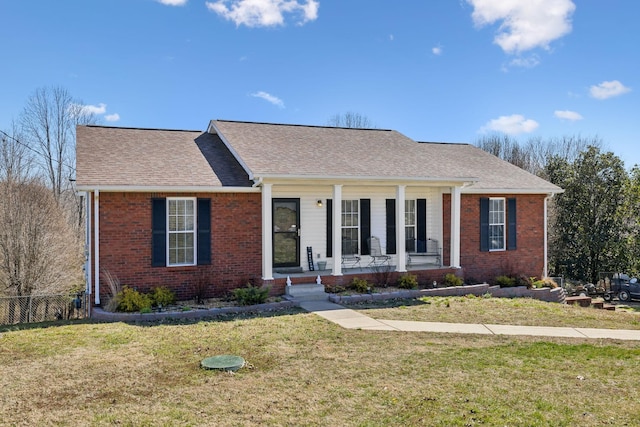 ranch-style home with covered porch, brick siding, fence, roof with shingles, and a front lawn