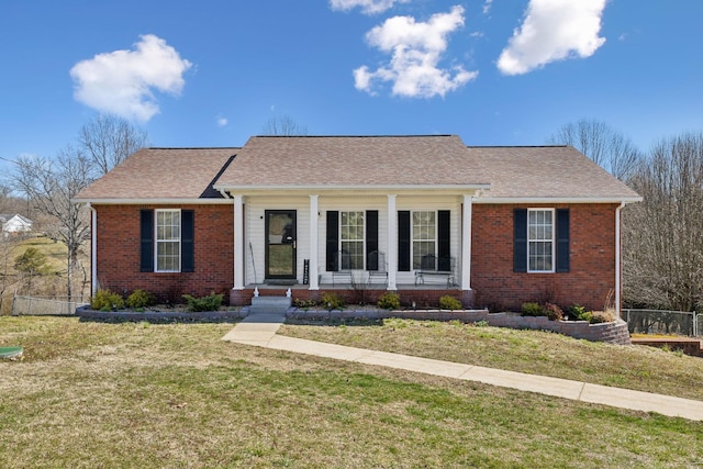 view of front of home with covered porch, fence, a front lawn, and brick siding