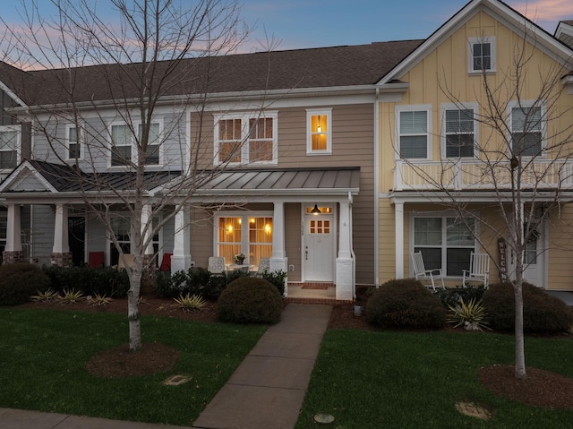 view of property with a shingled roof, metal roof, covered porch, a standing seam roof, and a front lawn