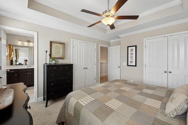 bedroom with a tray ceiling, crown molding, multiple closets, light carpet, and connected bathroom