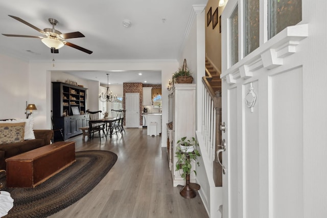 entryway featuring light wood-type flooring, crown molding, stairway, and ceiling fan with notable chandelier