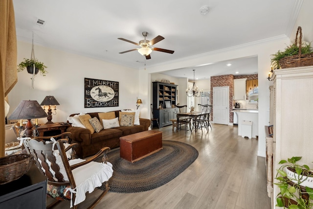 living area with ceiling fan with notable chandelier, light wood finished floors, and crown molding