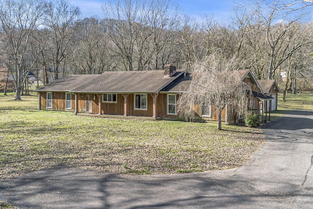 view of front facade featuring covered porch, driveway, a front lawn, and a chimney