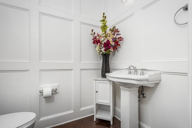 half bathroom featuring a decorative wall, toilet, and wood finished floors