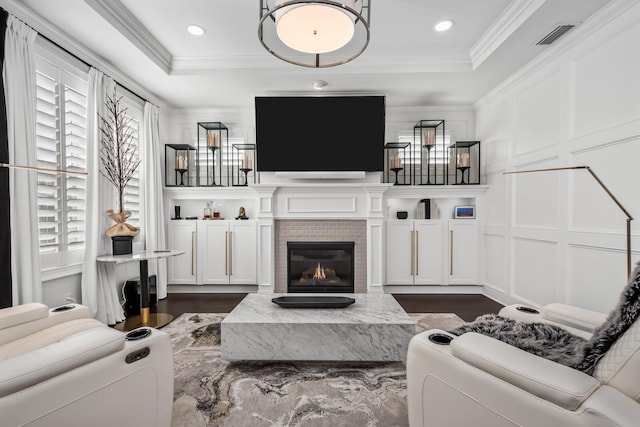 living area with crown molding, a tray ceiling, a glass covered fireplace, and a decorative wall