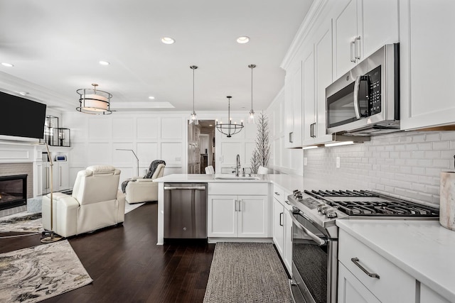 kitchen featuring a sink, open floor plan, appliances with stainless steel finishes, a glass covered fireplace, and crown molding