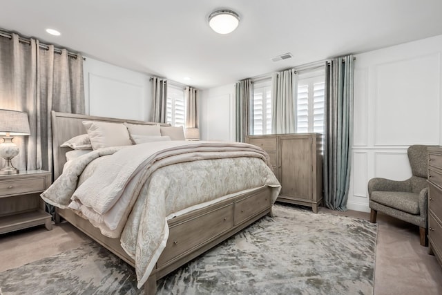 bedroom with light colored carpet, visible vents, and a decorative wall