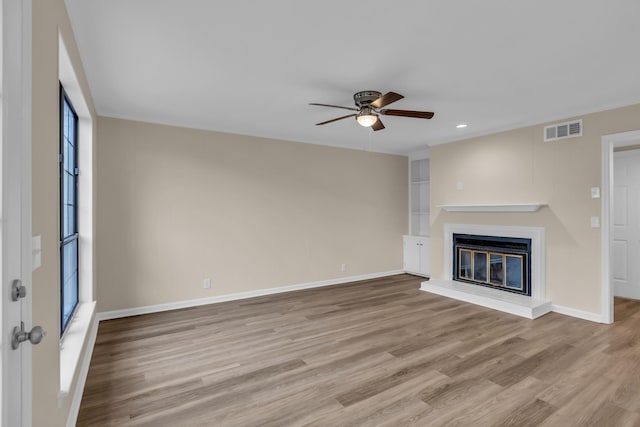 unfurnished living room with baseboards, visible vents, a ceiling fan, a glass covered fireplace, and wood finished floors