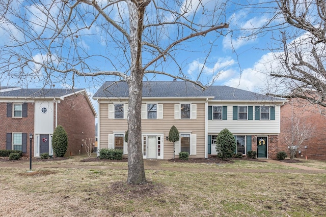 view of front of property with a shingled roof, a front lawn, and brick siding