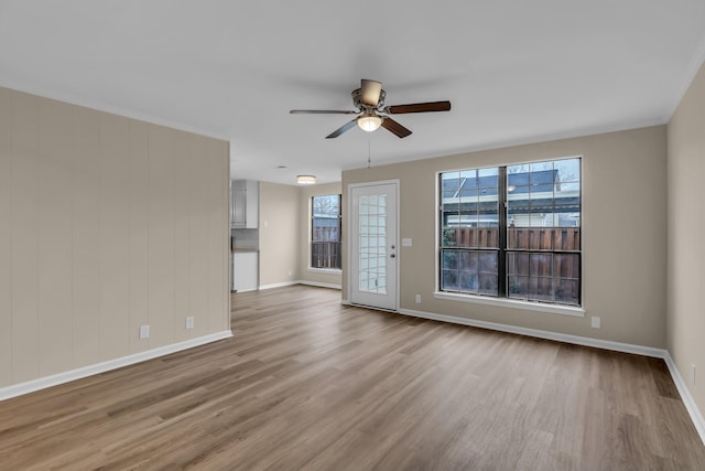 unfurnished living room with ceiling fan, crown molding, baseboards, and wood finished floors