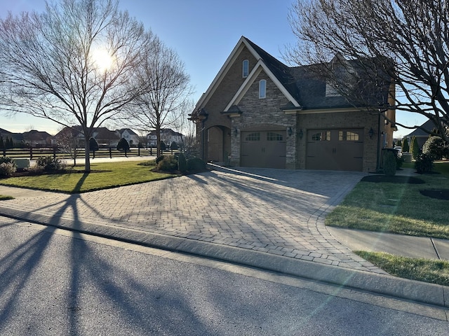 view of front facade with decorative driveway, fence, a garage, stone siding, and a front lawn