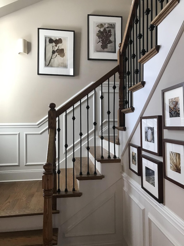 staircase featuring a decorative wall, wainscoting, and wood finished floors