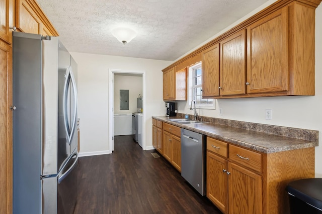 kitchen featuring a textured ceiling, a sink, appliances with stainless steel finishes, dark countertops, and dark wood finished floors