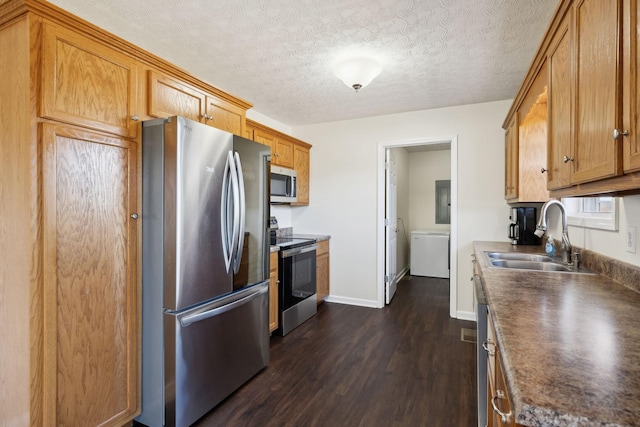 kitchen featuring dark wood-style floors, stainless steel appliances, dark countertops, a sink, and a textured ceiling