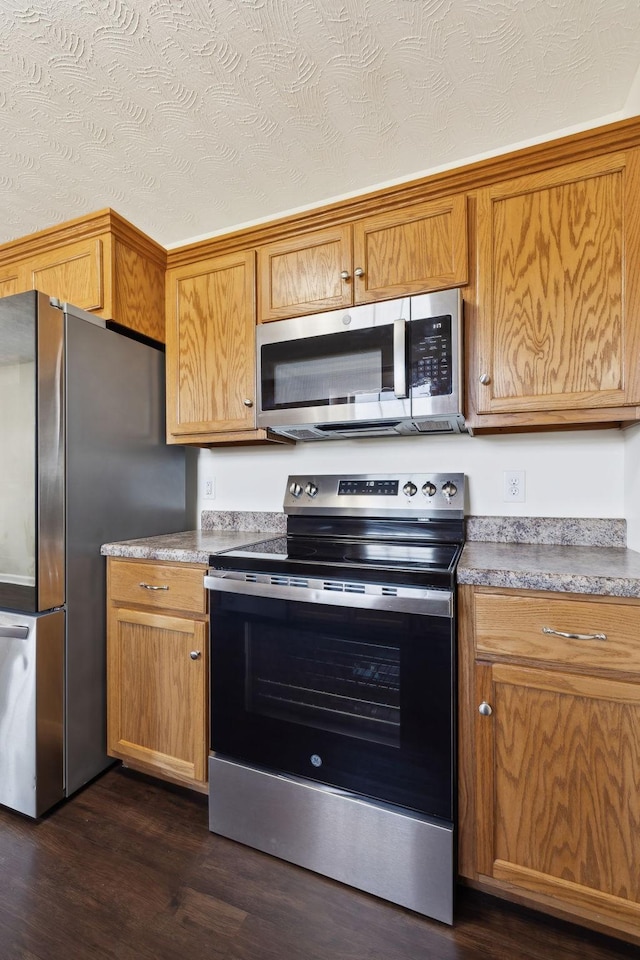 kitchen with a textured ceiling, stainless steel appliances, dark wood-type flooring, and brown cabinets