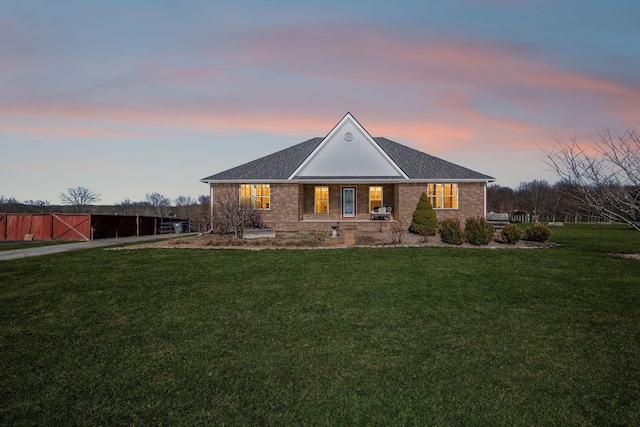 view of front of property featuring a shingled roof, brick siding, and a lawn