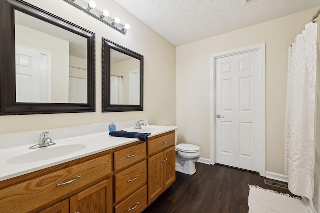 bathroom featuring double vanity, wood finished floors, a sink, and toilet