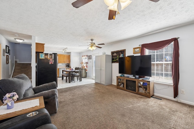 living area featuring ceiling fan, a textured ceiling, baseboards, and light colored carpet