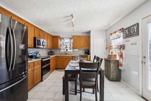 kitchen featuring brown cabinets, a sink, stainless steel appliances, light countertops, and backsplash