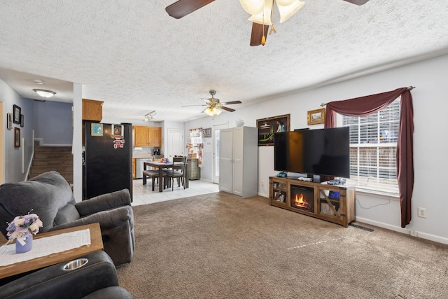 living room with a textured ceiling, baseboards, a ceiling fan, and light colored carpet