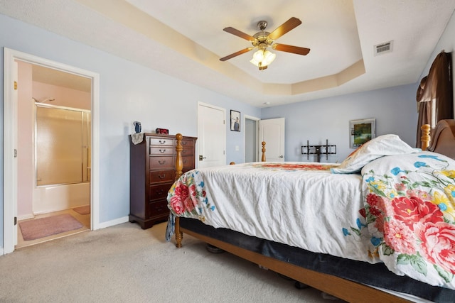 carpeted bedroom with a tray ceiling, visible vents, ceiling fan, ensuite bath, and baseboards