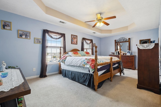 carpeted bedroom featuring ceiling fan, a raised ceiling, visible vents, and baseboards