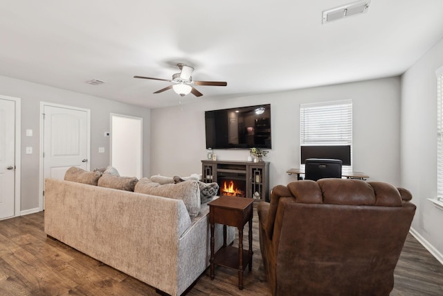 living area with visible vents, dark wood finished floors, a lit fireplace, and baseboards