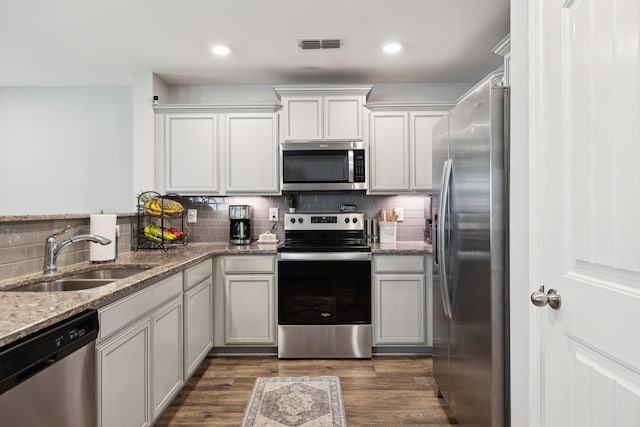 kitchen with appliances with stainless steel finishes, dark wood-type flooring, a sink, and tasteful backsplash