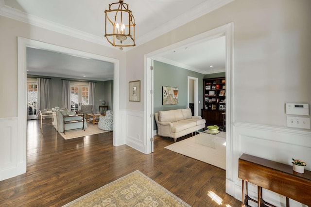 interior space featuring a wainscoted wall, crown molding, a decorative wall, wood finished floors, and a chandelier