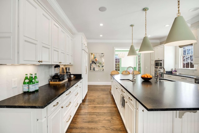 kitchen with an island with sink, ornamental molding, and a sink