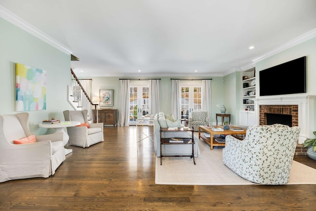 living area with built in shelves, ornamental molding, a brick fireplace, wood finished floors, and stairs