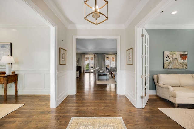 foyer entrance with dark wood-style flooring, a wainscoted wall, french doors, an inviting chandelier, and ornamental molding