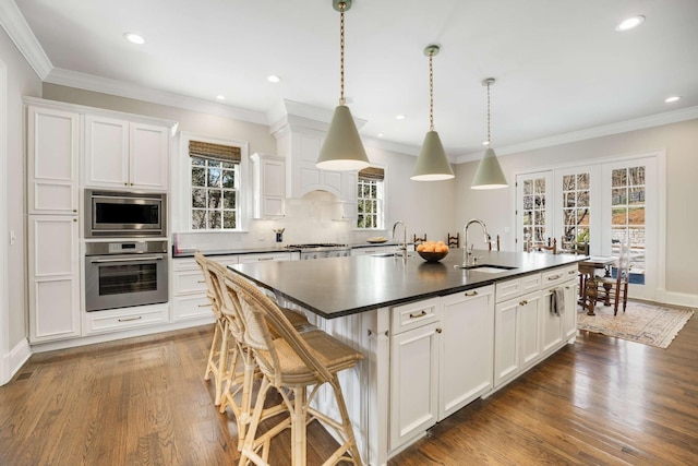 kitchen featuring dark wood-style flooring, a sink, appliances with stainless steel finishes, an island with sink, and dark countertops