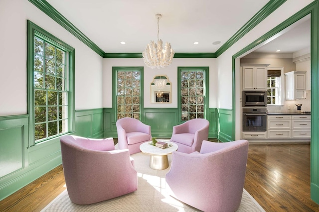 sitting room featuring an inviting chandelier, crown molding, wood finished floors, and a wainscoted wall