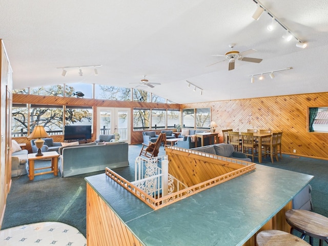 interior space with rail lighting, a ceiling fan, vaulted ceiling, wood walls, and a textured ceiling