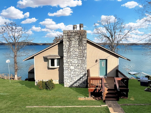 back of house with a yard, a chimney, and a water view