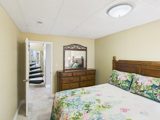 bedroom featuring baseboards, visible vents, a drop ceiling, and light tile patterned floors