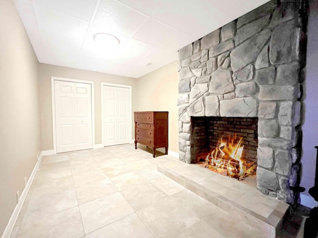 unfurnished living room featuring tile patterned flooring, a stone fireplace, and baseboards