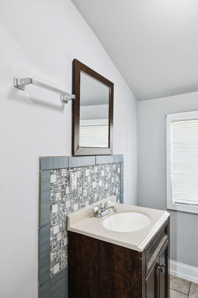 bathroom featuring baseboards, lofted ceiling, tile patterned flooring, vanity, and backsplash