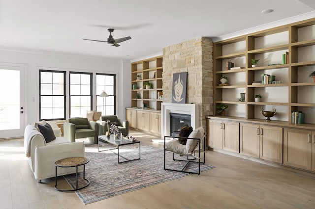 living area featuring light wood-style flooring, built in shelves, ceiling fan, and a glass covered fireplace