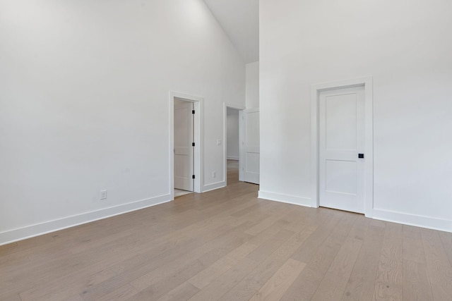 unfurnished bedroom featuring light wood-type flooring, high vaulted ceiling, and baseboards