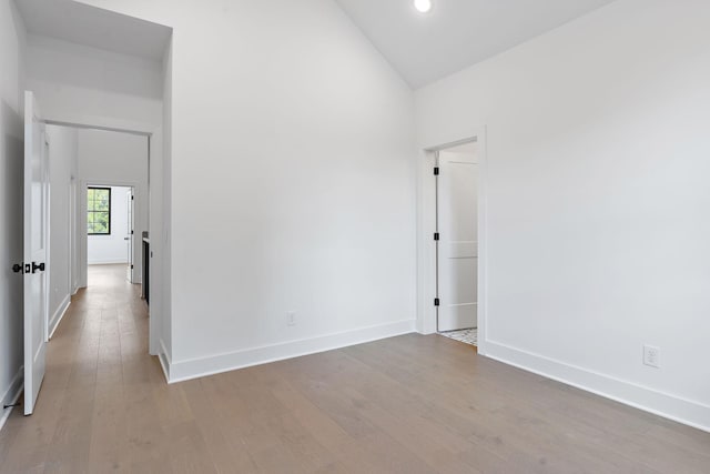 spare room with high vaulted ceiling, baseboards, and wood finished floors