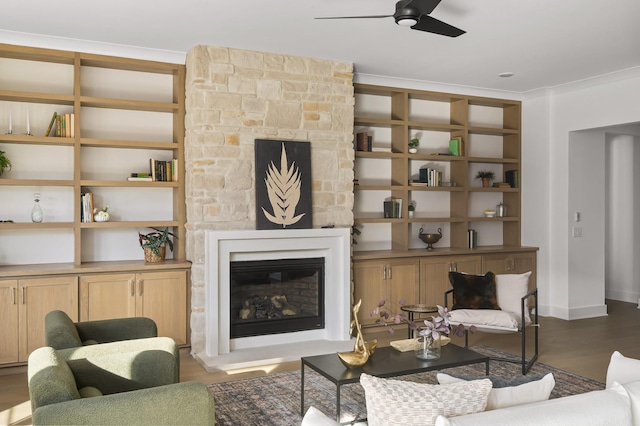 living area with built in features, a ceiling fan, a fireplace, and wood finished floors